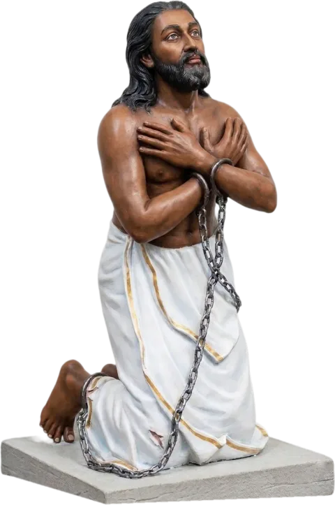 St Devasahayam Pillai statue kneeling in chains with his hands crossed on his chest and eyes raised to heaven, in a white mundu with a gold border, on a stone base
